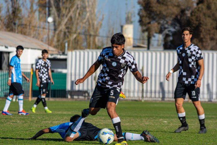 A group of young football players competing intensely during a match on a sunny day.