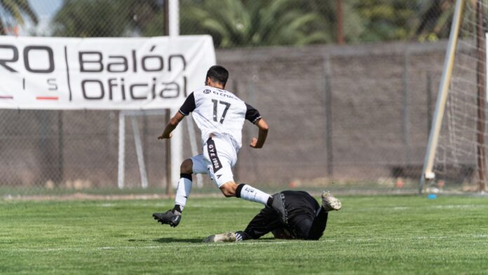 Dynamic soccer scene of a player evading a sliding tackle on the field.
