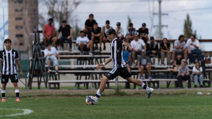 A soccer player in black and white jersey kicks the ball during a match with spectators in background.