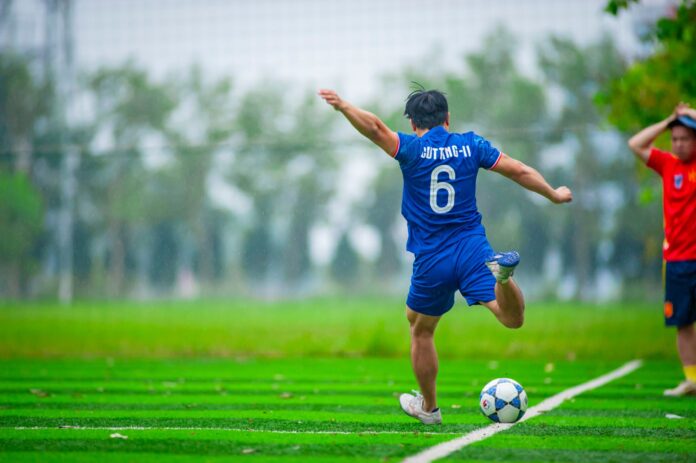 Energetic soccer player kicks ball on a lush field in Hanoi, Vietnam.